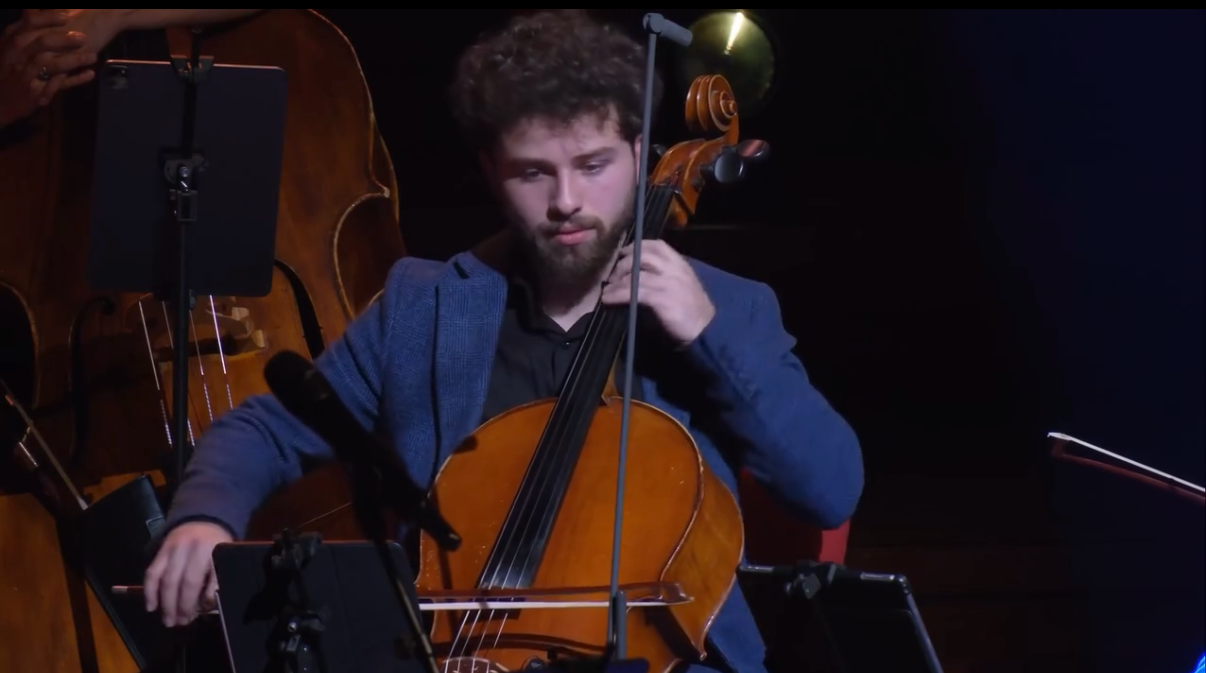 Qusai Naim playing cello on stage in a concert